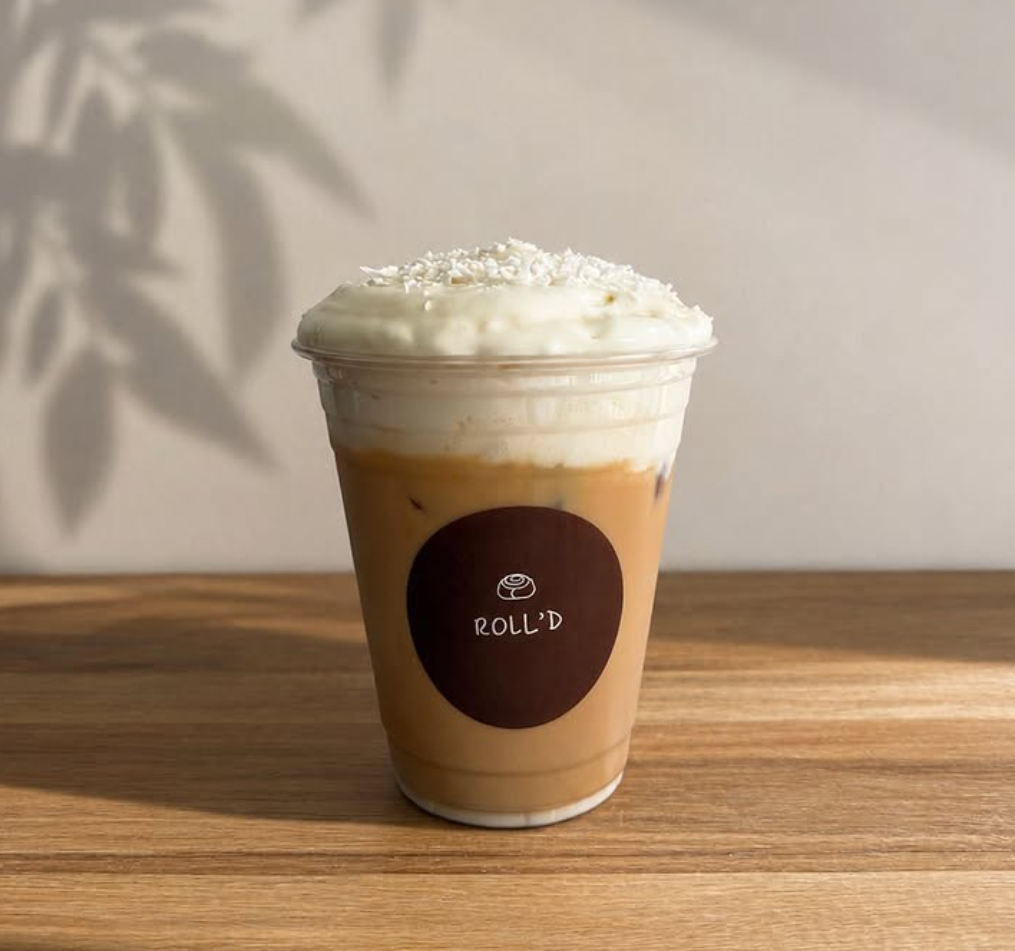 An iced latte topped with cloud foam and coconut shavings in a Roll'd branded cup